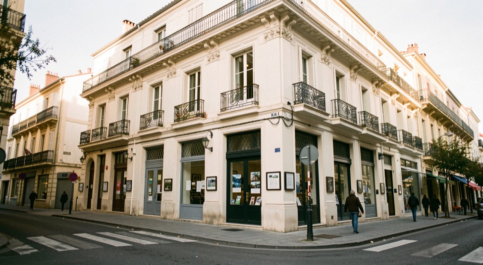 Salle de cinéma vide avant la séance, écran blanc encore éteint, file de fauteuils rouges en léger contre-jour sous les appliques murales